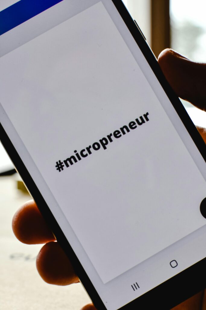 pexels-photo-6956224-6956224 Close-up of a hand holding a smartphone with the hashtag #micropreneur on screen, symbolizing entrepreneurship.